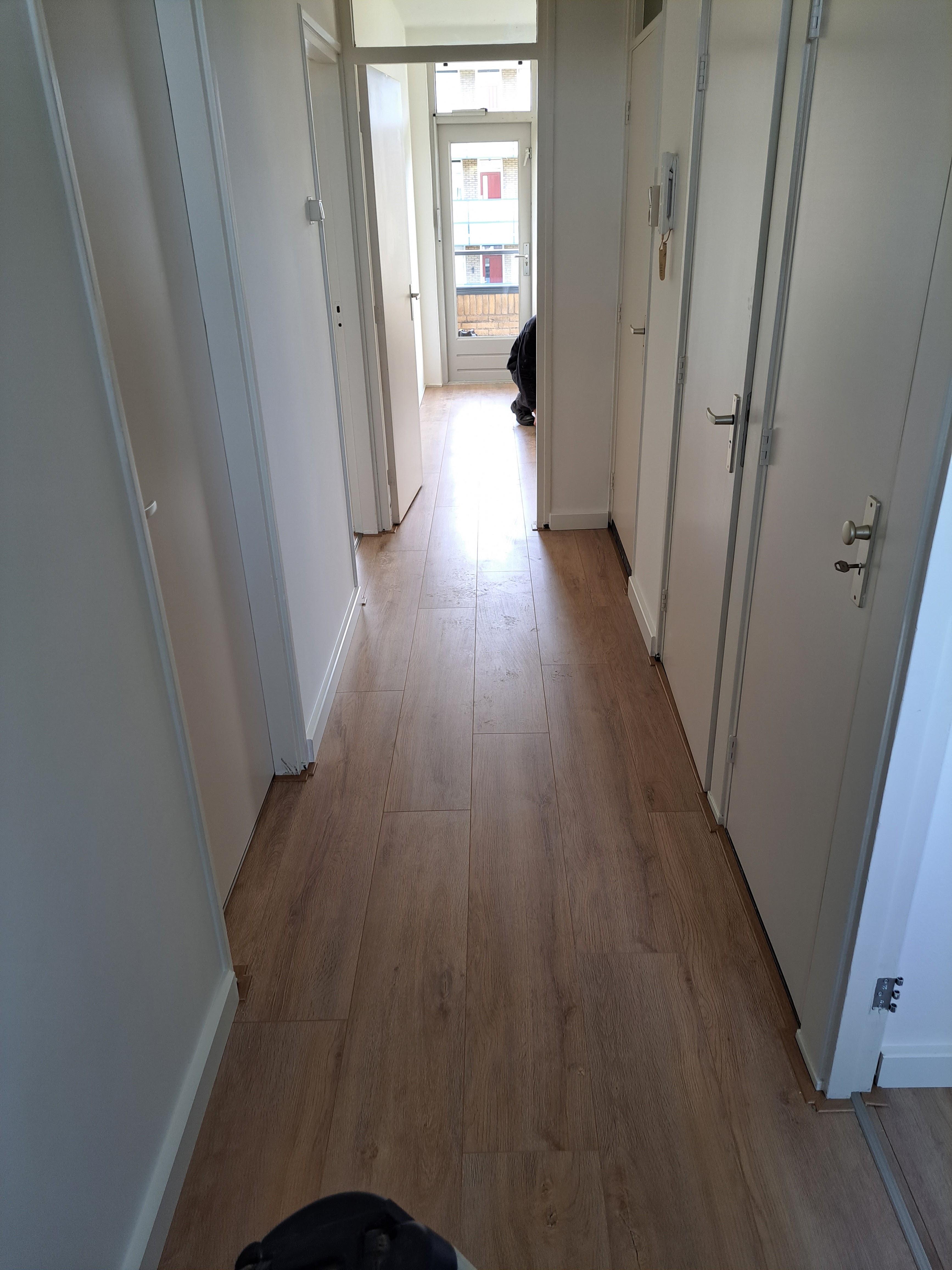 Lange gang met bruine laminaatvloer en witte deuren