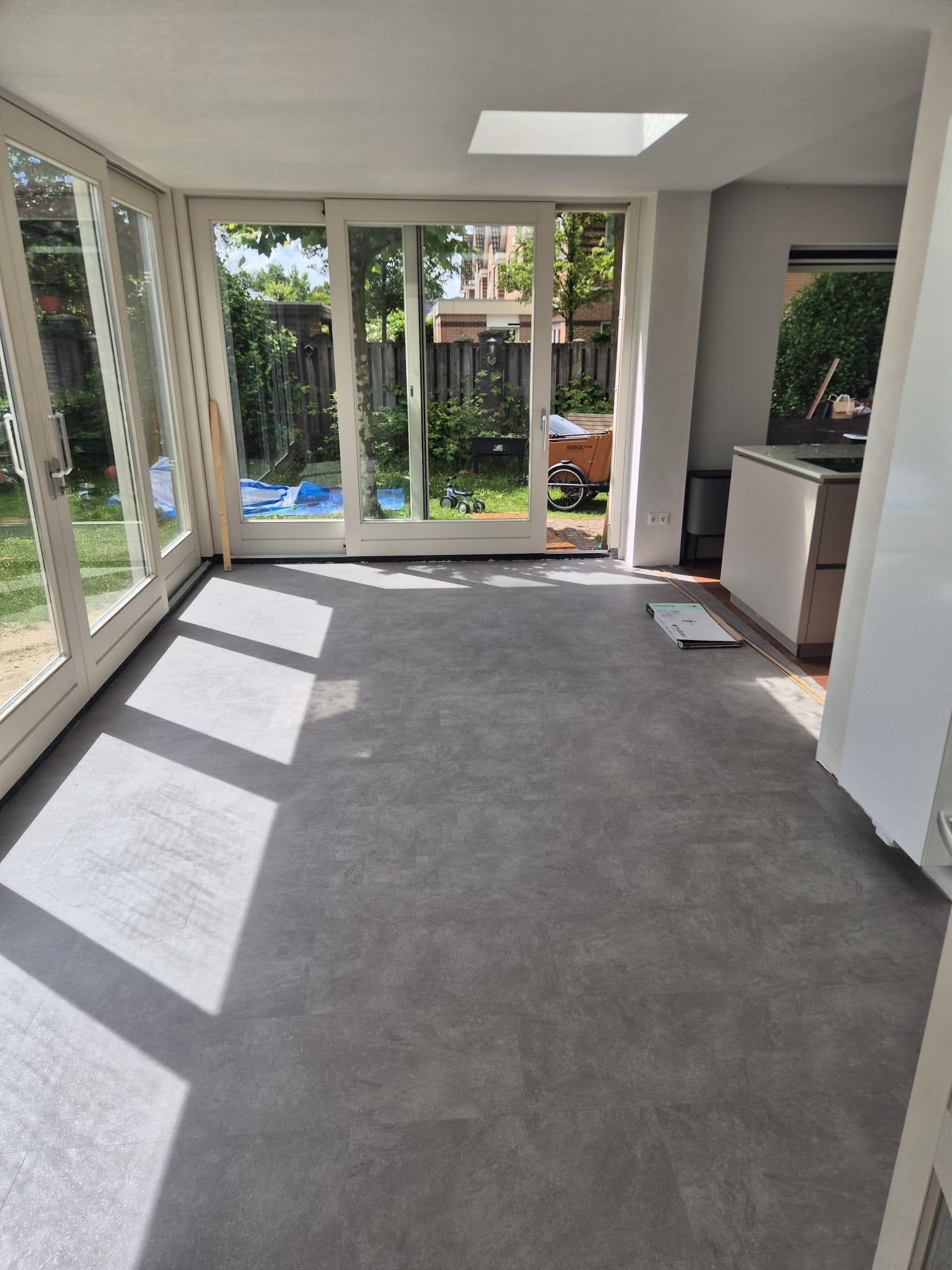 Grijze pvc vloer in een lichte serre met tuindeuren